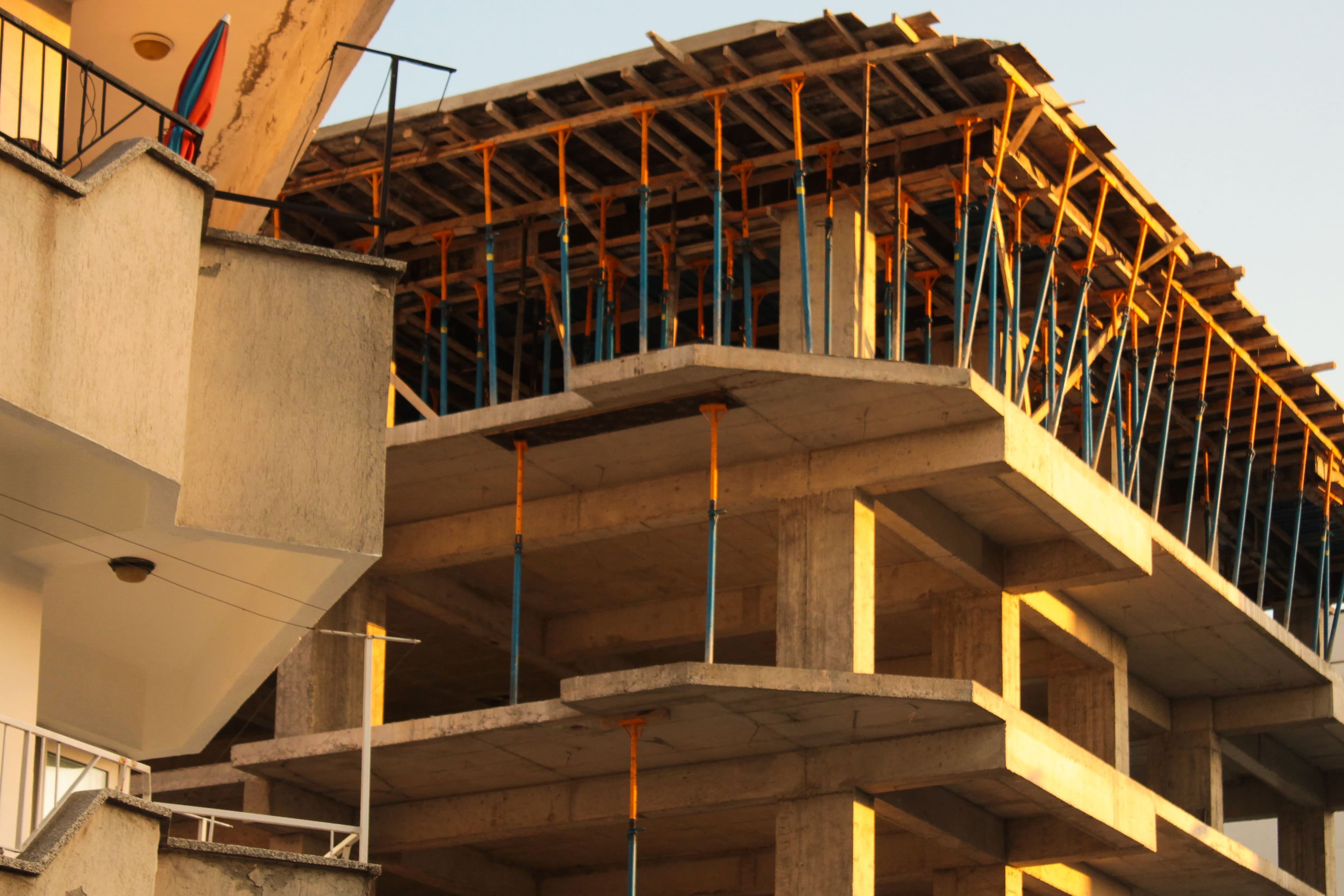 Concrete frame of a multi-storey building under construction, held up by orange and blue steel props